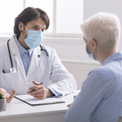 Geriatrician in medical mask talking with senior patient in office